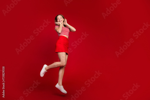 Full length photo of excited impressed girl wear striped top short skirt jumping high empty space isolated red color background