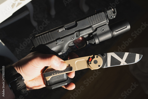 Tactical weapon, G19 pistol with a flashlight and a folding knife in a man’s hand.