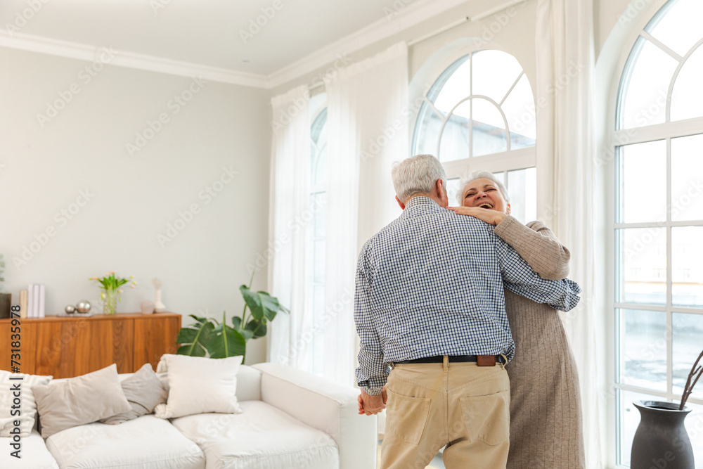 Obraz premium Keep moving. Romantic senior mature couple dancing to music together at home. Happy smiling family retired man woman husband wife having fun enjoying time together. Family moment love care
