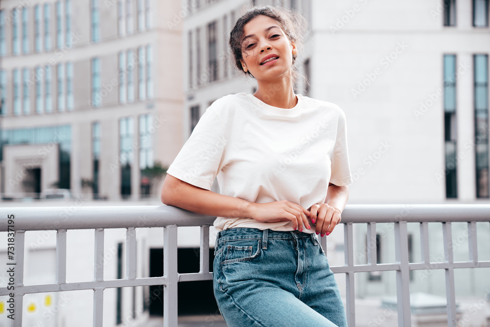 Young beautiful smiling hipster woman in trendy summer white t-shirt and jeans clothes. Carefree woman, posing in the street at sunny day. Positive model outdoors