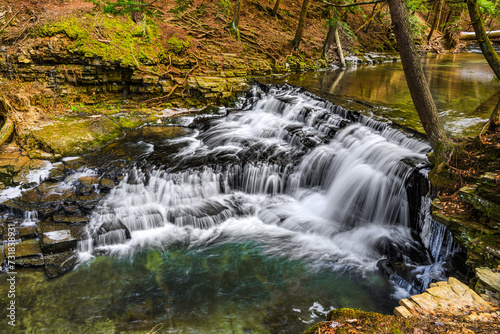 A partially frozen waterfall in late winter.  Water rushes over and down the rocks at Salt Springs State Park in Montrose  PA.  Heavy ice has already melted due to warmer temperatures.