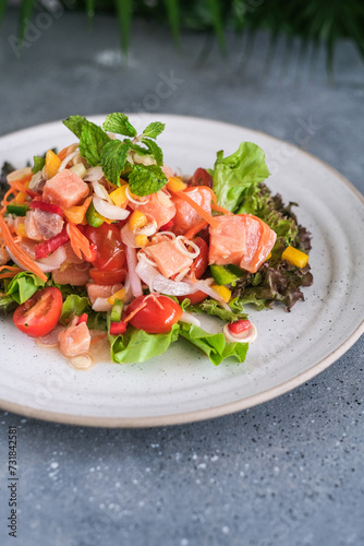 Tasty and fresh salad with raw salmon, greens, tomato, pepper, onion, carrot, olive oil.