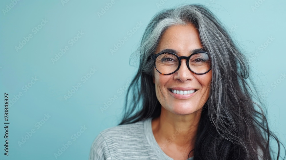 Smiling woman with gray hair and glasses wearing a gray top against a light blue background.