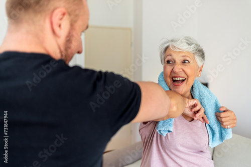 Cropped shot of a young man and old woman bumping elbows. Senior women and fitness trainer exercising together at home.