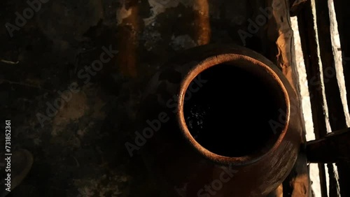 hands of elderly Latino man taking water from a clay container called tinaja with an aluminum glass inside a wooden house in a rural area