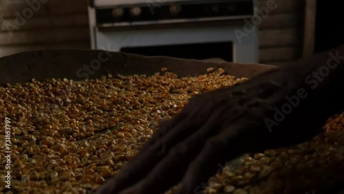 Hands of older Latino adult moving corn kernels in a rustic handmade wooden tray on wooden table inside a hut