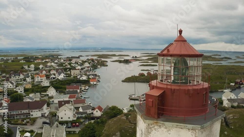 Cinematic Kvitsøy Island, white with red top Lighthouse slow rise, revealing harbour boats and village Ytstebohamn in the background North Sea cloudy skyes moving in over this isolated Island. photo