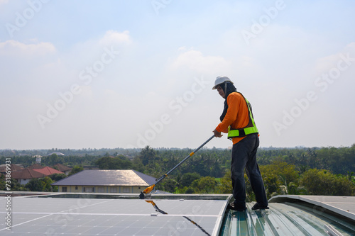 Professional worker cleans solar panels with brush and rinses with water on roof structure of construction factory. Technician uses a mop to clean dirt and dust, green electric power technology photo