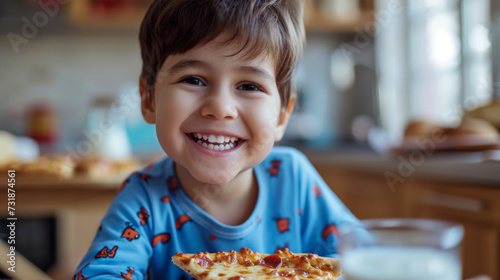 A smiling child in casual clothing is joyfully eating a slice of pizza, with a glass of milk on the table in a home kitchen setting.