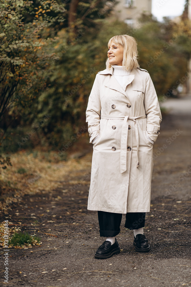 Aged woman wearing a beige coat standing in park Aged woman wearing a beige coat standing in park