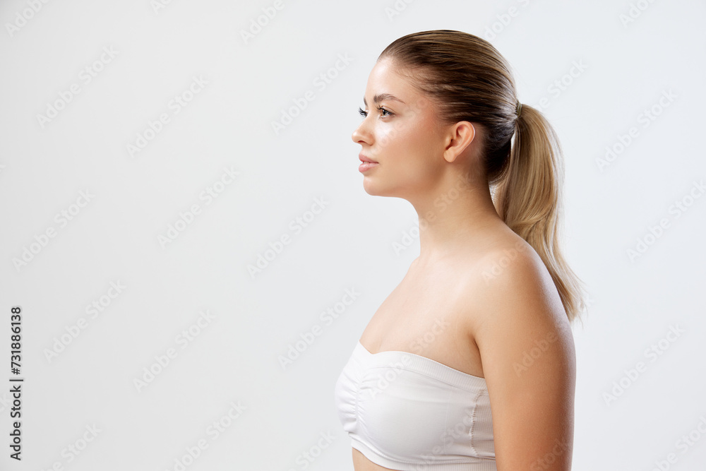 Profile of young woman with hair in ponytail, wearing strapless top against white background. Physical therapy and posture correction services. Concept of beauty, skincare, cosmetics and cosmetology Profile of young woman with hair in ponytail, wearing strapless top against white background. Physical therapy and posture correction services. Concept of beauty, skincare, cosmetics and cosmetology