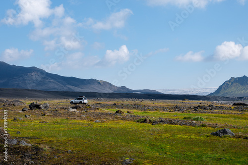 Amazing Icelandic landscape with snowy mountains, river, field and a car on a sunny day with Mýrdalsjökull glacier in the background. Famous Laugavegur hiking trail