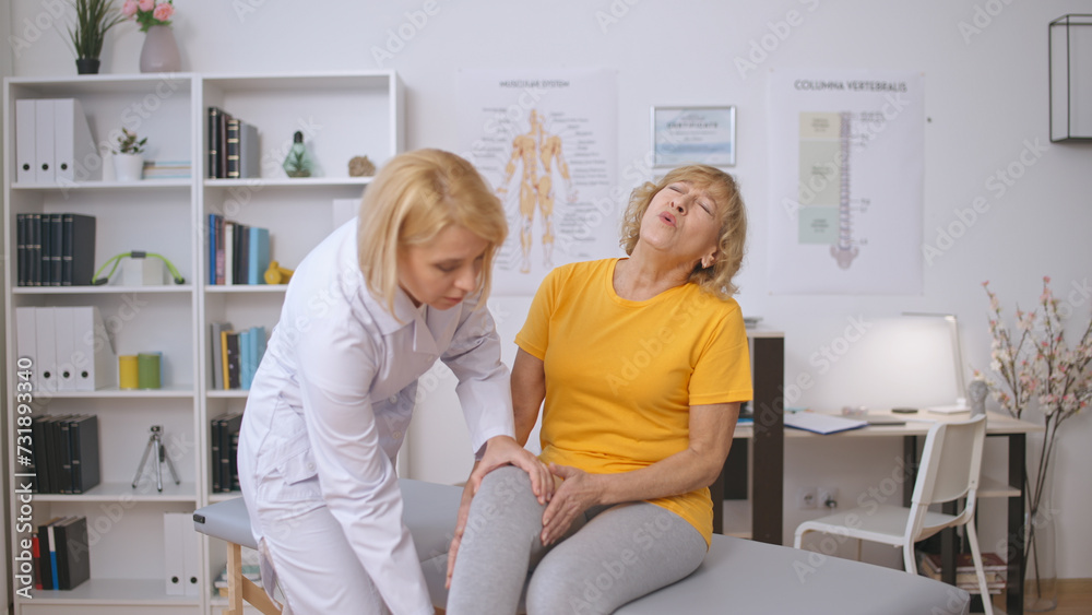 A woman traumatologist examines the sore knee of a female patient who is crying in pain A woman traumatologist examines the sore knee of a female patient who is crying in pain