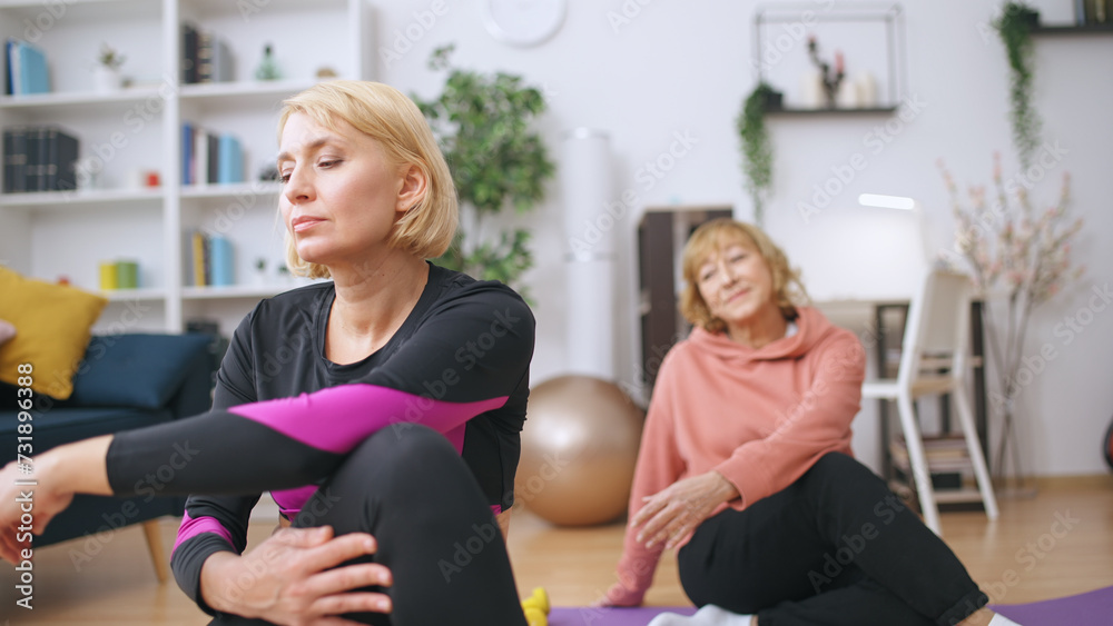 An adult daughter and her senior mother do stretching exercises together, focusing on fitness