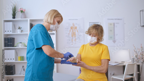 A nurse applies a medical band to a senior patient's injured hand, providing trauma treatment photo