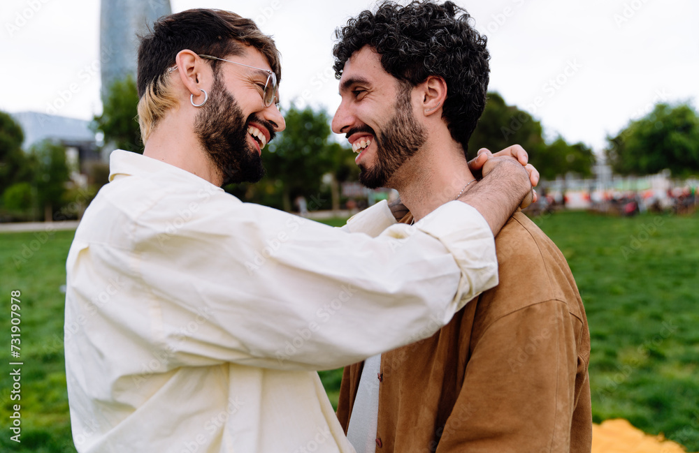Happy gay couple hugging in park with green lawn Happy gay couple hugging in park with green lawn