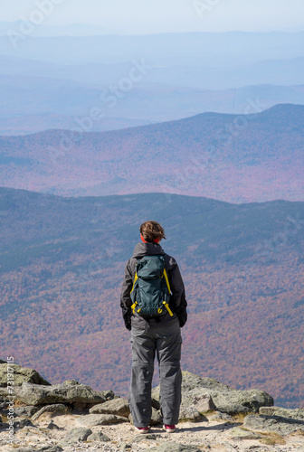 A woman stands on Mount Washington and watches the woods in a distance.