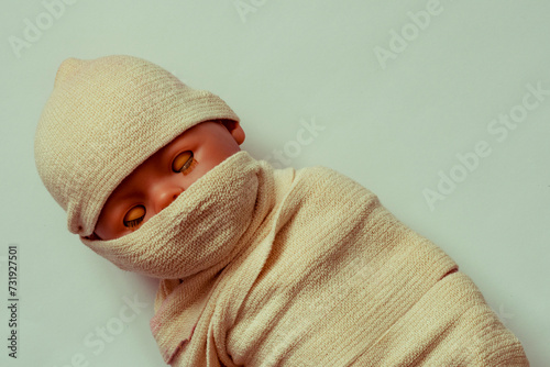 The doll the baby is wound with fabric. The body of the child is shrouded in a shroud. The concept the Muslim dead man. A mummy on a  background. close-up. corpse, dead. Funeral concept, before burial