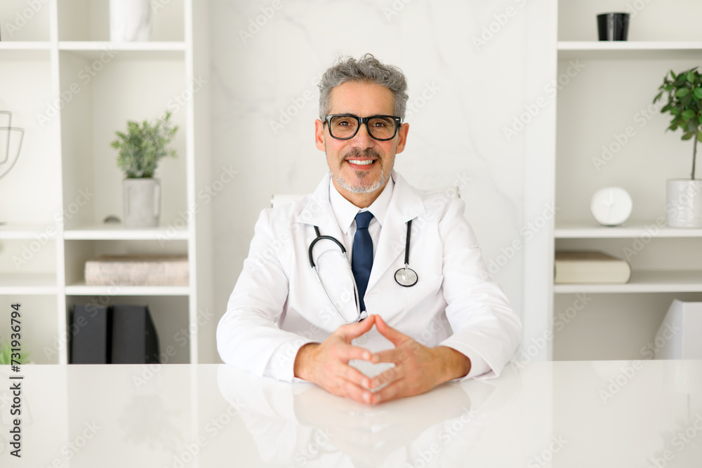 A friendly senior doctor looking directly at the camera, his hands open in a welcoming gesture, inviting trust and communication in a modern healthcare setting. Portrait of experienced MD on workplace A friendly senior doctor looking directly at the camera, his hands open in a welcoming gesture, inviting trust and communication in a modern healthcare setting. Portrait of experienced MD on workplace