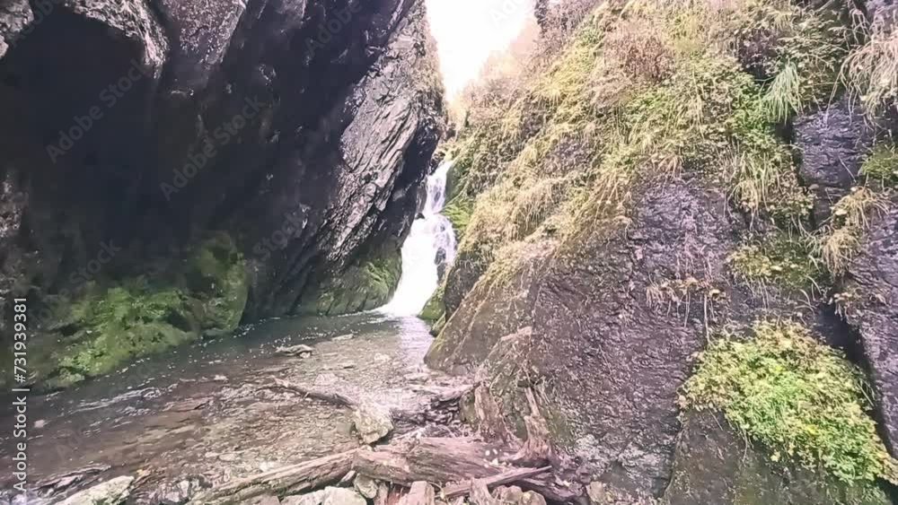 A small waterfall flows from a crevice in the mountains forming a rushing river on a cloudy autumn day. Estyuba River, Altai, Siberia, Russia.