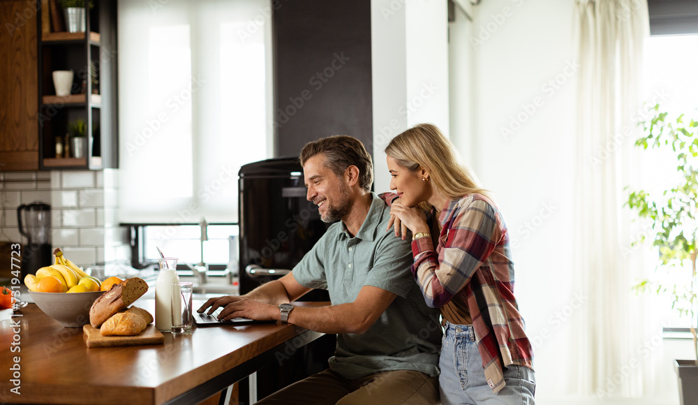 Morning Bliss: Couple Enjoying a Healthy Breakfast and Laptop Time in a Sunlit Kitchen Morning Bliss: Couple Enjoying a Healthy Breakfast and Laptop Time in a Sunlit Kitchen