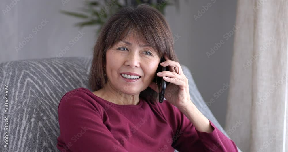 Cheerful mature woman enjoying talking using smartphone relaxing sitting at home near bright window light.