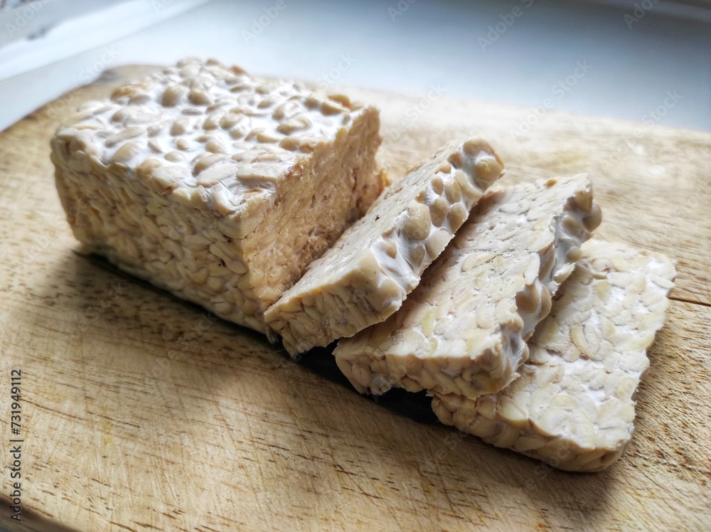 Sliced raw soybean tempeh, a typical Indonesian food on a cutting board. Sliced raw soybean tempeh, a typical Indonesian food on a cutting board.