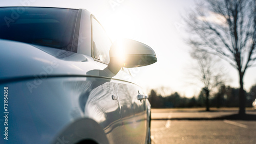 Low angle of a white car with sun shining over the rear view mirror