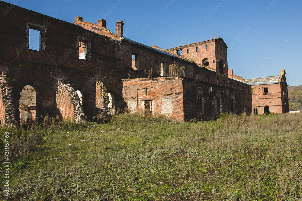 Ruins of an old factory building with large arched windows and a blue sky in the background