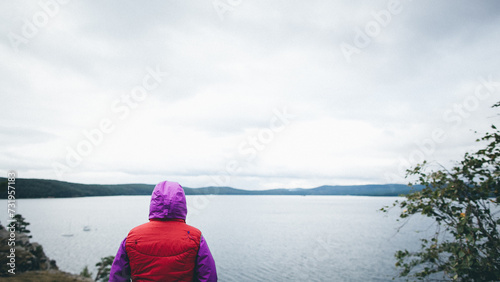 Woman in red and purple jacket looking out at lake on an overcast day