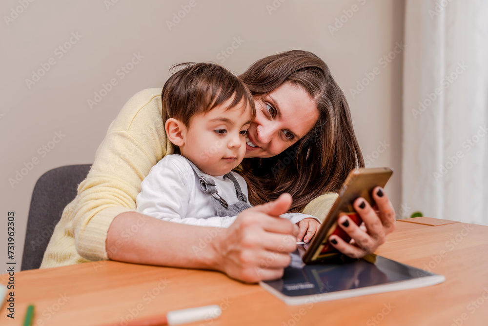 Smiling mother and toddler son using the smartphone to watch cartoon at home Smiling mother and toddler son using the smartphone to watch cartoon at home