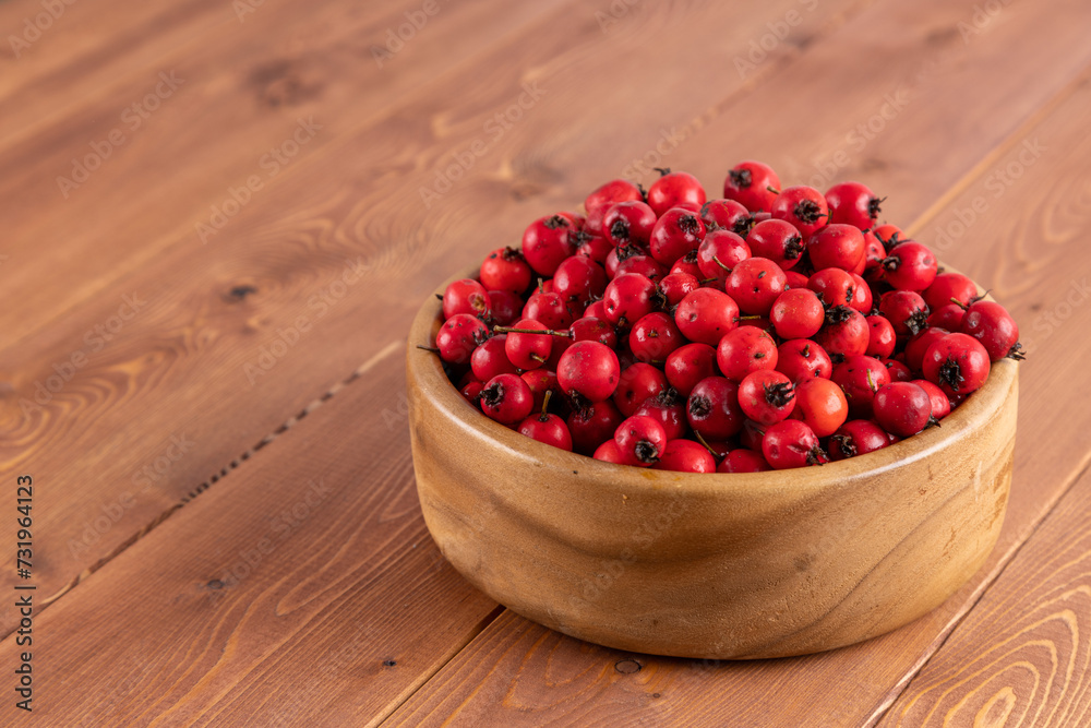 red hawthorn berries in wooden bowl on flat wooden surface. red hawthorn berries in wooden bowl on flat wooden surface.