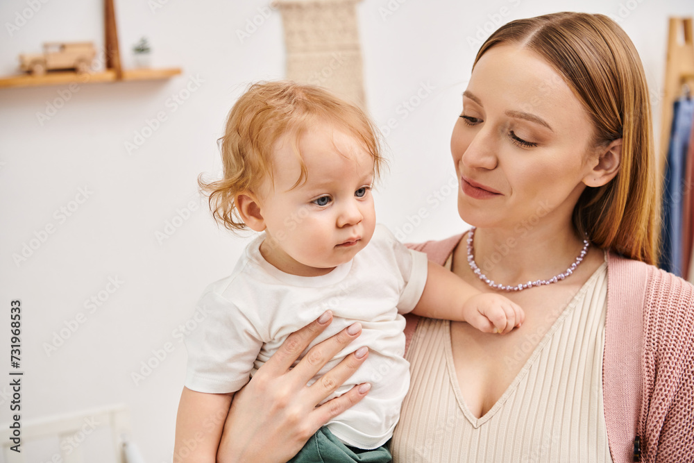 cheerful attractive woman holding little toddler son in hands in nursery room, happy motherhood