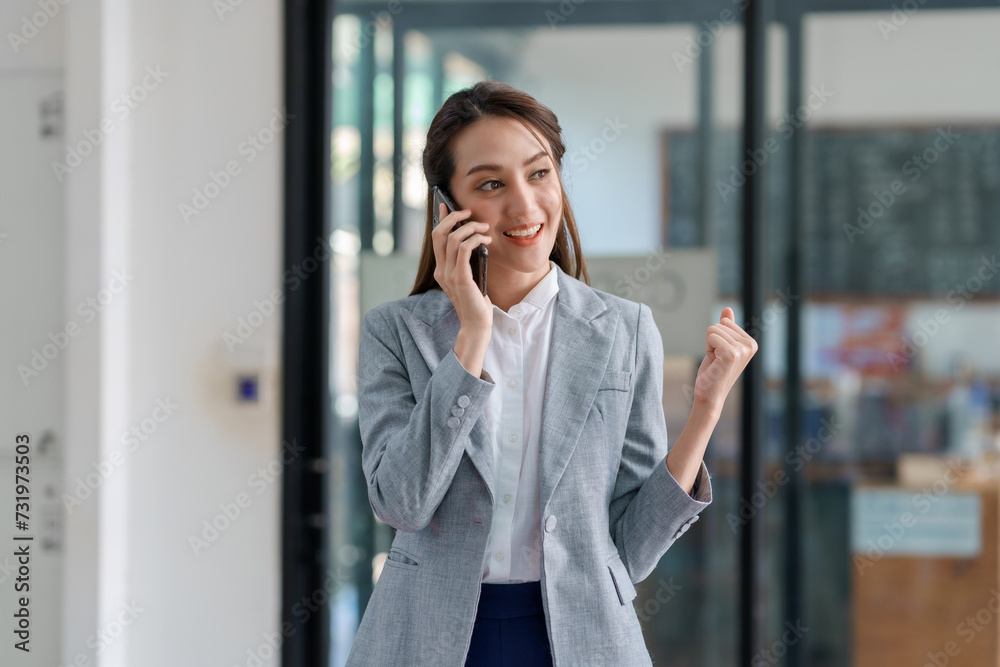 Cheerful asian businesswoman in a gray suit having a pleasant conversation on her mobile phone in a office corridor. Cheerful asian businesswoman in a gray suit having a pleasant conversation on her mobile phone in a office corridor.