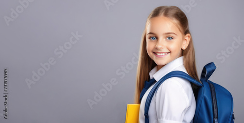 Happy smiling 10-year-old girl with long blonde hair, wearing school uniform with blue backpack, ready to go to school, isolated gray background. Smiling, white teeth, looking at the camera. Copy