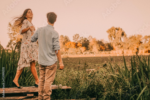 Happy, smiling couple in a green park with the sunset light, hugging, kissing, walking hand in hand, and lying on the ground and grass, representing their love outdoors and sincere love © nehuen