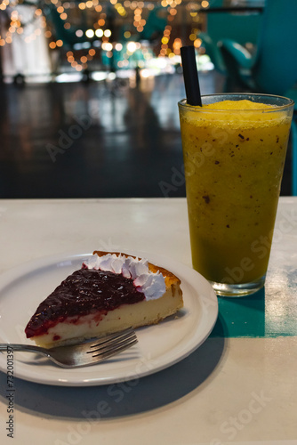 exquisite red fruit cake and whipped cream accompanied by a refreshing mango juice drink on a wooden table inside a restaurant, cafe