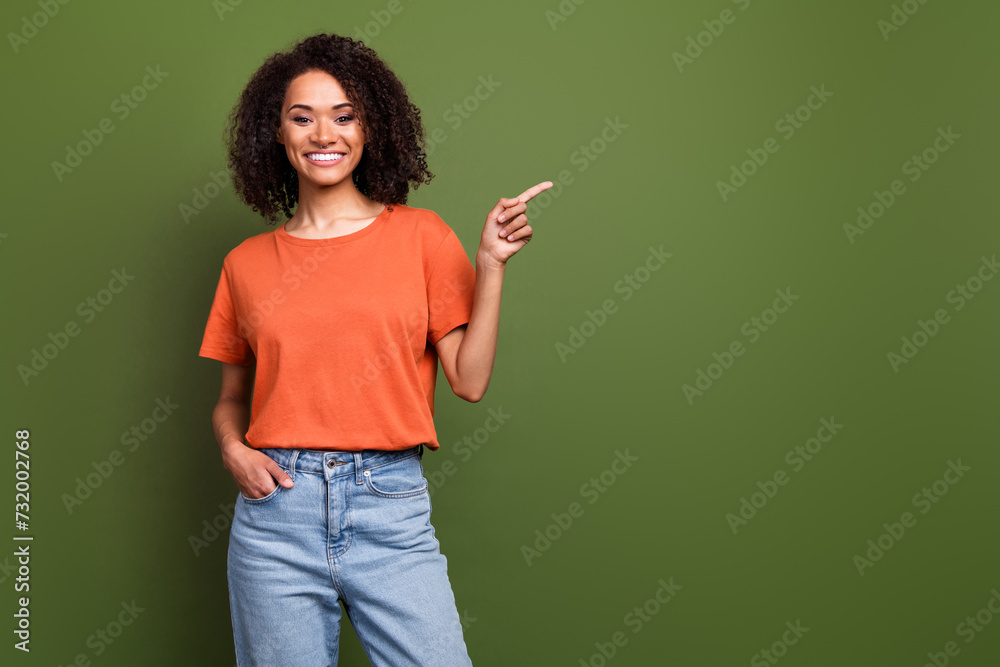 Photo of cute shiny woman wear orange t-shirt showing finger empty space isolated green color background Photo of cute shiny woman wear orange t-shirt showing finger empty space isolated green color background