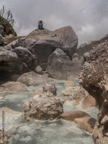 mujer joven sentada en una piedra usando abrigos mientras esta en un rio termal  photo