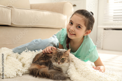 Cute little girl with cat lying on carpet at home. First pet