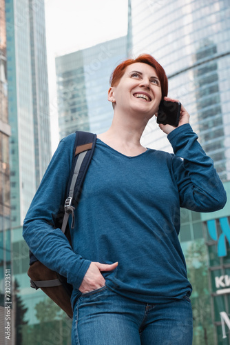 woman with red hair stands in a modern business district and talking on the phone © Galina