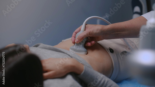 Caucasian woman undergoes ultrasound diagnostics of abdominal organs in modern clinic or hospital. Professional doctor does stomach sonography check up procedure using advanced medical equipment.