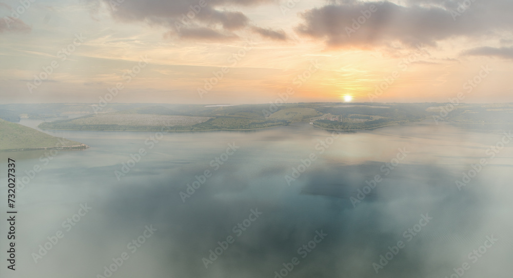 Hazy sunrise over a calm lake with gentle hills in the background. Eco optimism concept.