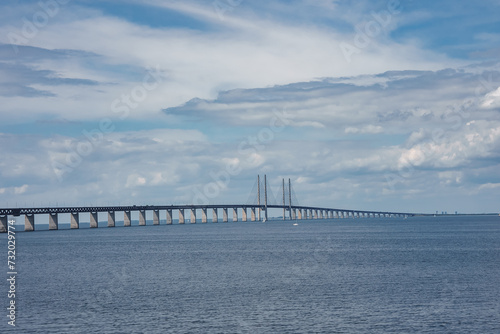 The Oresund Bridge, connecting Copenhagen, Denmark, with Malmo, Sweden, is captured on a clear day, its pylons and cables reflecting on the calm strait below.