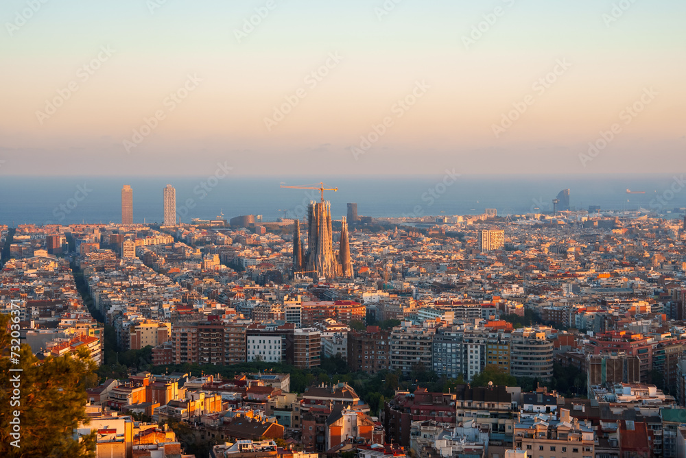 Panoramic view of Barcelona at golden hour with the Sagrada Familia center stage, surrounded by the Eixample district's grid streets and a mix of modern and historical architecture.