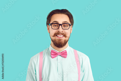 Portrait of funny male nerd hipster in stylish colored clothes on light blue background. Guy with mustache and beard in shirt, suspenders and glasses with funny expression looks at camera. 