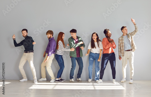 Full length portrait of a funny happy overjoyed group of young diverse friends students or colleagues in casual clothes having fun standing together in a row on a gray wall background.