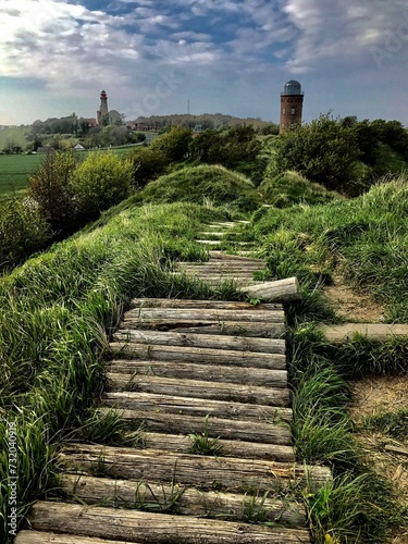 sea ​​lighthouse on the seashore against the background of a road made of wooden logs on a green hill