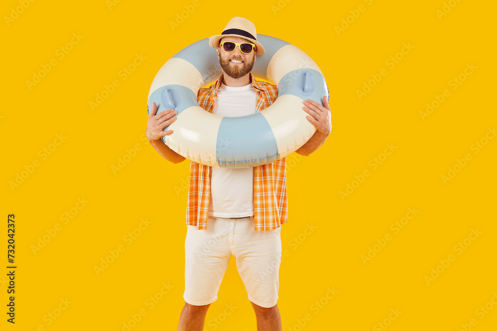 Happy, smiling man in beach attire against an orange background, holding an inflatable ring, enjoying vacation. Joy of summer holidays and travel, as the man enjoys a carefree moment.
