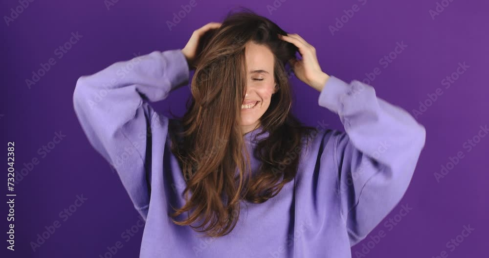 Cheerful happy joyful young woman wear purple hoody, brunette loose hair cheerfully throws. Smiling face. Happy woman fix hair, look funny and funky isolated on violet background.